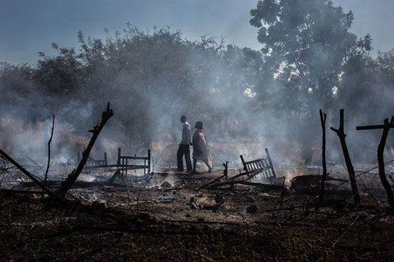 Affiche Expositions Tensions, Photo de Camille Delage d'un couple debout au milieu de leur village en cendres.